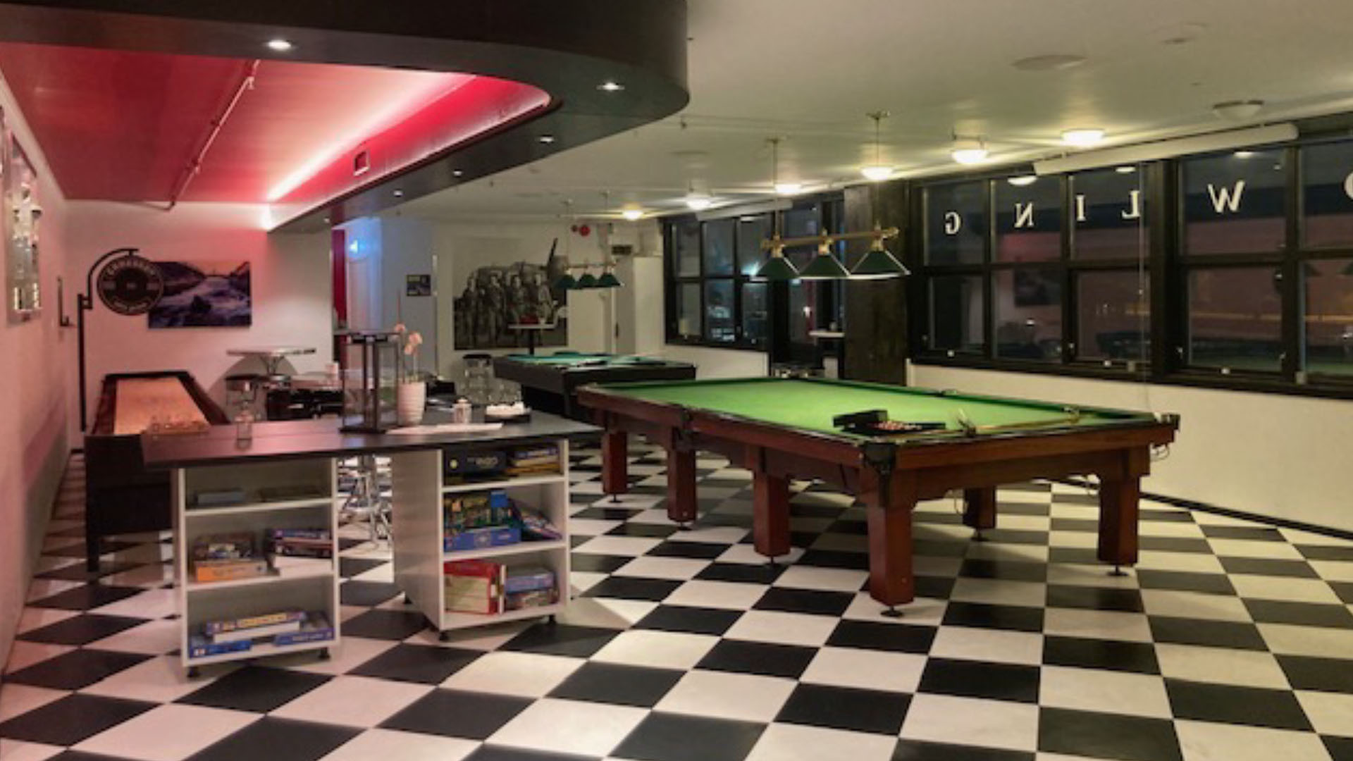 Aktivitetslounge med sjakkbrett-gulv, biljardbord og neon-rødt taklys