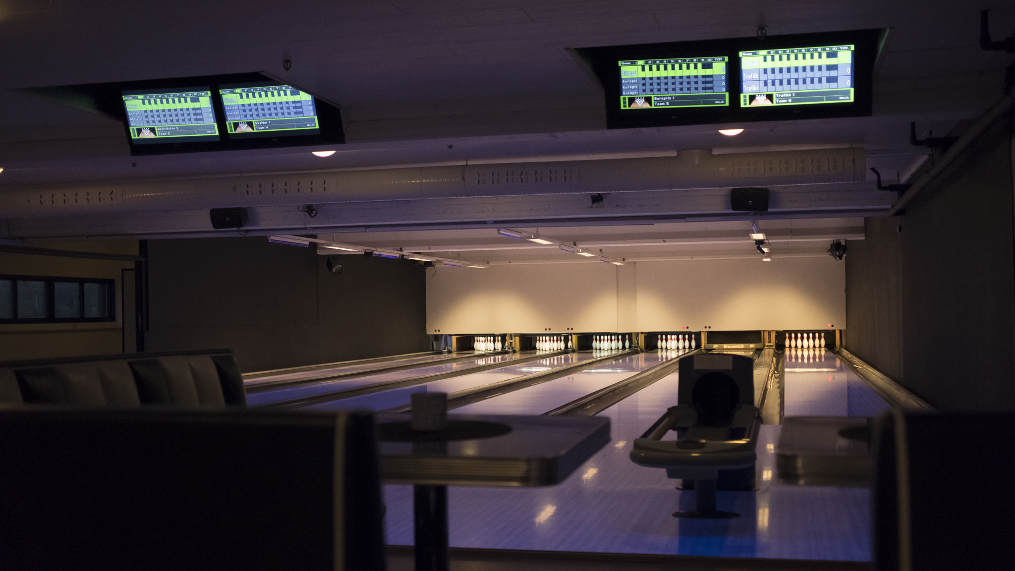 Bowlinghallen i kveldslys — banene strekker seg innover, scoringsskjermer hengt fra taket